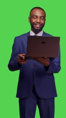 Dikey video: Kamera üzerinde dizüstü bilgisayarla çalışan başlangıç yöneticisinin ön görünümü ve kablosuz bilgisayar ile çevrimiçi ağ sayfasına göz atmak. Genç işletme çalışanı taşınabilir internet sitesi kullanıyor