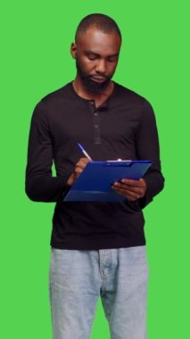 Dikey video: Yeşil ekran arkaplanı üzerinden notlar alan, dosyalara pano ile bilgi yazan sıradan insanların ön görünümü. Genç model stüdyoda yeni fikirler üretiyor, profesyonel.