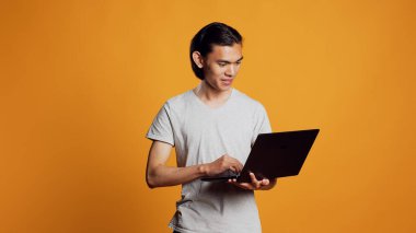 Asian model using laptop on camera, browsing internet website on wireless pc. Young carefree adult working with protable computer, scrolling through social media app and online browser.