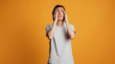 Sick male model dealing with painful headache, feeling tired and stressed on camera. Young ill person suffering from serious migraine, acting unhappy in studio and rubbing temples.