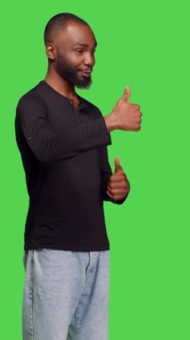 Dikey video: Kamera önünde, başarılı bir jest ve anlaşma gösteren sıradan bir insanın yan görüntüsü. Genç adam yeşil ekranın arkasında onaylı sembol gibi duruyor.