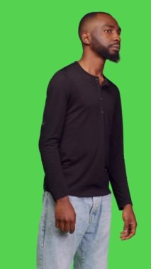 Dikey video: Erkek modelin, izole edilmiş yeşil ekran arkaplanındaki bilgileri düşünceli ve bekleyerek düşünceli bir şekilde düşünmesi. Sabırlı genç adam yeni fikirler üretiyor.