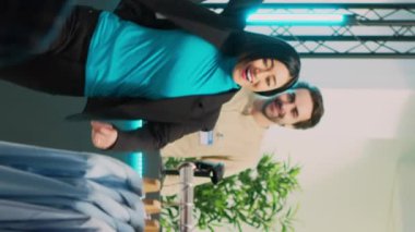 Dikey video: Asyalı müşteri dans hareketleri yapıyor ve kendini aptal hissediyor, moda butik kasasından modaya uygun giyim ile ayrılıyor. Alışveriş torbalarıyla, alışveriş merkeziyle dans eden mutlu, gülümseyen kadın..