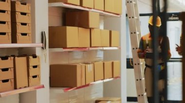 Personel ekibi depodaki malları ve kargoyu kontrol ediyor. Depodaki dizüstü bilgisayar ve dosya listesini kullanıyor. Ürünleri karton paketlerde düzenleyen iki adam raflarda, malları kontrol ediyor..