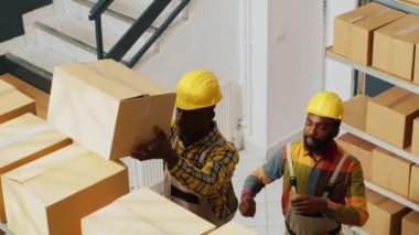 Depoda ürün lojistiği üzerinde çalışan bir grup iş arkadaşı depodaki ürün paketlerini kontrol ediyor. Depo çalışanlarından oluşan neşeli bir ekip mal listesiyle stok sayımı yapıyor..