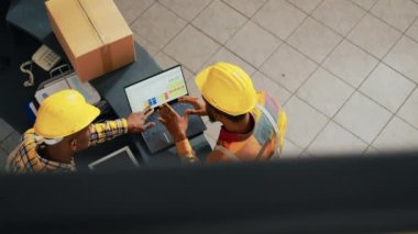 Kağıt üzerinde lojistik listesini inceleyen insanlar dizüstü bilgisayarla ve panoyla stok envanterinde çalışıp raflardaki malları kontrol ediyorlar. Yapım için siparişlerle birlikte sevkiyat planlama. El kamerasıyla..