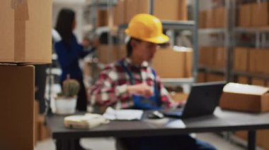 Asyalı adam depoda mal kalitesini kontrol ediyor. Diz üstü bilgisayarla sevkiyat ve teslimat üzerinde çalışıyor. Dağıtım yönetimi için envanter analizi yapan genç işçi, küçük işletme konsepti.