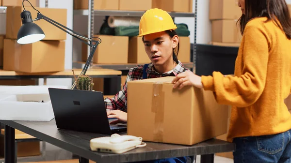 アジアの男は 棚に箱に商品を整理し ラップトップで収納室の在庫を行っています 倉庫スペースで働く若い大人が注文の出荷 製品の流通を計画する — ストック写真