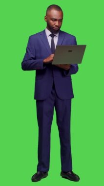Dikey video: Modern çalışanın ağı taramak için dizüstü bilgisayar kullanmasının ön görüntüsü, tam vücut yeşil ekranının üzerinde duran çevrimiçi web sitesine bakmak. Genç iş adamı kablosuz bilgisayarla çalışıyor.