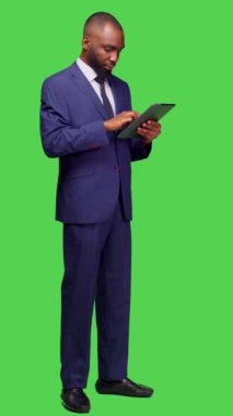 Dikey video: Tablet üzerinde internet sitesine göz atan modern çalışanın yan görüntüsü, tam vücut yeşil ekran arkaplanı üzerinde çevrimiçi ağ sayfası ile çalışıyor. Ofis takımında genç bir yetişkin, elinde aletle.