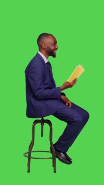 Dikey video: Sandalyeye oturmuş kitap ya da roman okuyan genç iş adamlarının boş zaman aktiviteleri için kurgusal hikayelere odaklandıkları profil. Kendine güveni tam bir girişimci edebiyat okuyor.