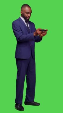 Dikey video: Akıllı telefonda video oyunu oynayan neşeli iş adamının yan görüntüsü, yeşil ekran arkaplanı üzerinden online oyun mücadelesinin keyfini çıkarıyor. Genç teknik direktör oyun yarışmasında kendini neşeli hissediyor