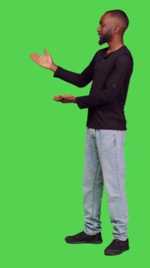 Dikey video: Afro-Amerikan bir adamın reklam için stüdyoda reklam oluşturması, reklam için sol ya da sağ tarafı göstermesi. Kot pantolon ve gömlek giymiş genç bir erkek model.