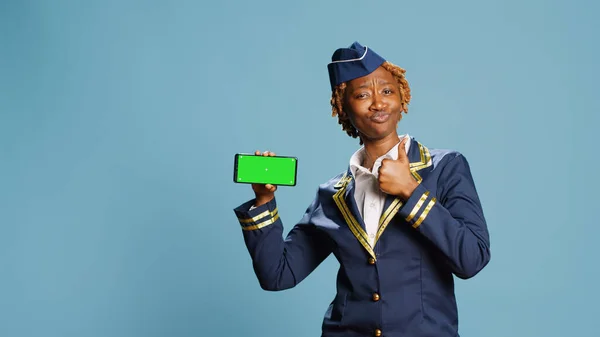 緑の画面でスマートフォンを保持している若い航空ホステスは カメラに隔離されたモックアップとクロマキーディスプレイを示しています 女性飛行士メンバー見ます黒テンプレート上の青の背景 — ストック写真