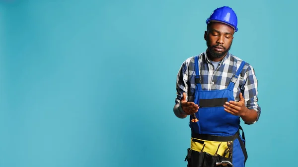 Professional builder almost fainting being wobbly, standing over blue background. Male construction worker feeling light headed with looney tunes cartoons stars on studio camera.
