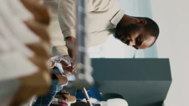 Dikey video: Mağazadaki müşterilere giysi gösteren kadın işçi, alışveriş merkezinde satışta olan modern malları arıyor. Genç mağaza asistanı butikte gündelik kıyafetlere bakıyor.
