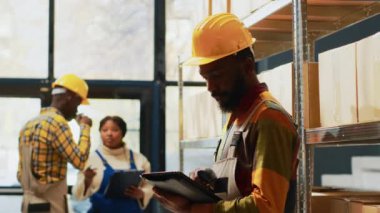 Depo çalışanı, depoda envanter sayımı yapmak için tarayıcı ve dijital tablet kullanarak barkodları depoda tarıyor. Depoda raflarda ürünlerle çalışan genç bir çalışan..