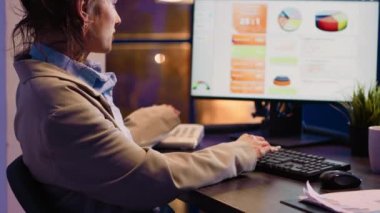 Female entrepreneur chatting on landline phone call at night with coworkers, talking about financial report with graphs and analytics. Employee using phone working after hours on development.