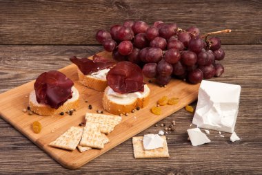 Stüdyo fotoğraf ahşap arka plan üzerinde jambon, kraker, üzüm ve beyaz peynir