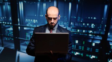 Sistem mühendisi dizüstü bilgisayarla sunucu teşhisi koyuyor, modern büyük veri merkezinde duruyor. Profesyonel ana bilgisayar donanımı üzerinde çalışan bilişim teknisyeni. Üçayak atışı.
