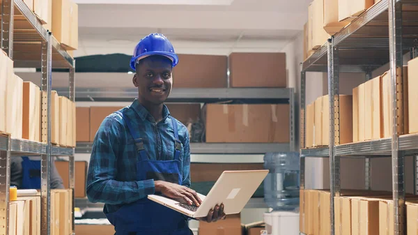 仓库员工在货架上计数货物箱 在分发产品前检查笔记本电脑上的库存清单 在工作服中使用计算机进行库存和后勤工作的年轻人 — 图库照片