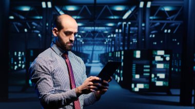 Sistem yöneticisi veri merkezindeki donanımı tabletle etkinleştiriyor, sunucu odasındaki modern sunucuları analiz ediyor. Erkek altyapı uzmanı ana bilgisayar sistemini inceliyor. Üçayak atışı.