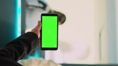 Dikey video: Asyalı asistan telefonda izole edilmiş yeşil ekran gösteriyor, krom anahtar şablonlu akıllı telefon görüntüsü kullanıyor. Kadın çalışan tutma aygıtı boş model ve kopyalama alanı, giyim mağazası
