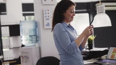 Kadın işçi internet sitesinde cep telefonuyla geziniyor, iş ofisinde çalışıyor. Genç girişimci şirket gelişimi için şirket raporlarını planlamak için akıllı telefonu kullanıyor. El kamerasıyla..