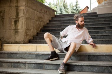 Moda dövmeli ve sakallı adam şehirde poz veriyor.