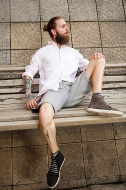 Sakallı hippi bankta yatıyor. Biçim ve moda