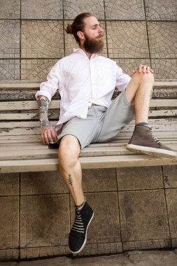 Bankta yatan sakallı, dövmeli hippi. Biçim ve moda