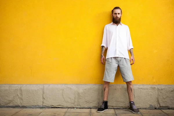 Cool Tattooed bearded hipster on yellow wall posing outdoor
