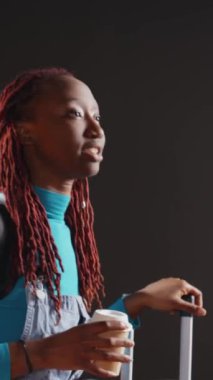 Dikey video: Elinde kahve bardağıyla uçak bekleyen neşeli kişi, şehirden ayrılıp şehir merkezine gitmeye hazırlanıyor. Genç bayan uluslararası seyahate çıkmadan önce serinletici bir şeyler içiyor. El bilgisayarı