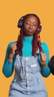 Dikey video: Afrikalı Amerikalı kız hava öpücüğü gönderiyor ve kulaklıkla müzik dinliyor, stüdyoda flört ediyor ve romantik davranıyor. Neşeli mutlu kadın dans ediyor ve neşeli hissediyor, romantizm işareti.