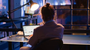 Female employee planning corporate analytics at night, working late in office to create financial report. Caucasian businesswoman analyzing financial investment to work on profit growth.