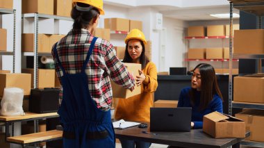 Stok lojistiği için paketleri açan bir grup insan depo alanındaki envanterleri kontrol ediyor. Asyalı işçiler ve girişimciler sevkiyat yönetimi ve küçük işletmeler üzerinde çalışıyorlar.