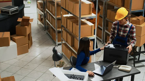 女企业主检查笔记本电脑上的产品库存 准备在仓库分发 做质量控制和在货架上装纸板箱的年轻妇女 — 图库照片
