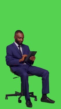 Dikey video: Afro-Amerikan bir adamın internet sitesini karıştırıp internet üzerinden dijital tablet ile ilgili iş bilgileri ararken yan görüntüsü. Takım elbiseli genç işadamı oturuyor.