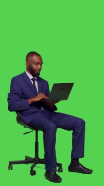 Dikey video: Şirket çalışanının iş planı üzerinde çalışmak için dizüstü bilgisayar kullanması, stüdyoda resmi takım elbise giymesi. Genç yönetici kablosuz bilgisayarda internet sayfasına göz atıyor, tam