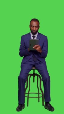 Dikey video: Çevrimiçi web sitesinde dijital tablet kullanarak tüm vucüt yeşil ekran arkaplanını tarayan genç girişimcinin ön görüntüsü. İş adamı İnternet ağı web sayfasında geziniyor