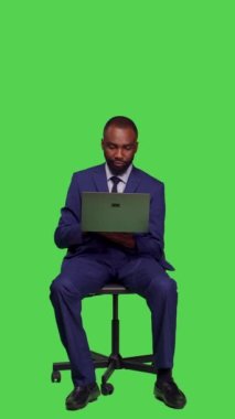 Dikey video: Şirket çalışanının iş planı üzerinde çalışmak için dizüstü bilgisayar kullanması, stüdyoda resmi takım elbise giymesi. Genç yönetici kablosuz bilgisayarda internet sayfasına göz atıyor, tam