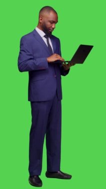 Dikey video: Modern çalışanın ağı taramak için dizüstü bilgisayar kullanmasının yan görüntüsü, tam vücut yeşil ekranının üzerinde duran internet sitesine bakması. Genç iş adamı kablosuz bilgisayarla çalışıyor.