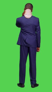 Dikey video: Yaralı iş adamının takım elbise giymesi ve boyun tasmasının tüm yeşil ekranın önünde durması. Genç bir çalışan yaralandıktan sonra acı çekiyor, kırık için tıbbi destek.