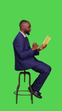Dikey video: Ofis çalışanının profili sandalyede oturup kitap üzerine roman okuması, kurgusal hikayelerden büyülenmesi, boş zaman aktivitelerinden etkilenmesi. Erkek şirket yöneticisi yeşil ekranda edebiyat okuyor
