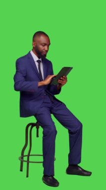 Dikey video: Çevrimiçi web sitesinde dijital tableti tam yeşil ekran arkaplanı üzerinde kullanarak genç girişimcilerin yan görünümü. İş adamı İnternet ağı web sayfasında geziniyor, resmi