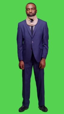 Dikey video: Yaralı iş adamının takım elbise giymesi ve boyun tasmasının tüm vücudun yeşil ekranının önünde durması. Genç bir çalışan yaralandıktan sonra acı çekiyor, kırık için tıbbi destek.