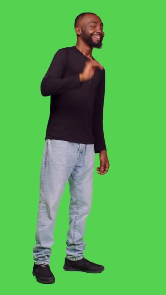 垂直录像 一个非洲裔美国人向工作室里的人挥手 在镜头前打招呼或告别的侧面画面 年轻模特儿笑着向站在全身绿色屏幕上的人致意 — 图库视频影像