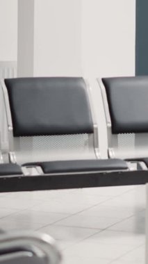 Dikey video: Klinikteki resepsiyon masası, sandalyeli ve sigorta broşürlü boş hastane lobisi. Acil servisteki bekleme salonu randevularını kontrol etmek için kullanılır.