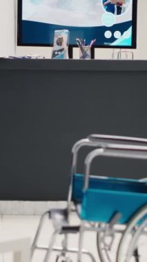 Dikey video: Tekerlekli sandalye ve koltuklarla donatılmış boş hastane resepsiyonu, sağlık sigortasına yardımcı olacak sağlık broşürleri. İyileşme tesisinde engelli dostu bekleme odası.