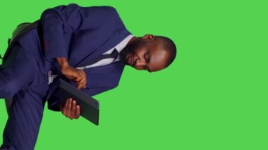Dikey video: Stüdyoda sandalyede oturan dijital tablet kullanarak sosyal medya sayfasında kayan erkek girişimcinin yan görüntüsü. Modern aygıtlarda online ağ taraması yapan genç girişimci